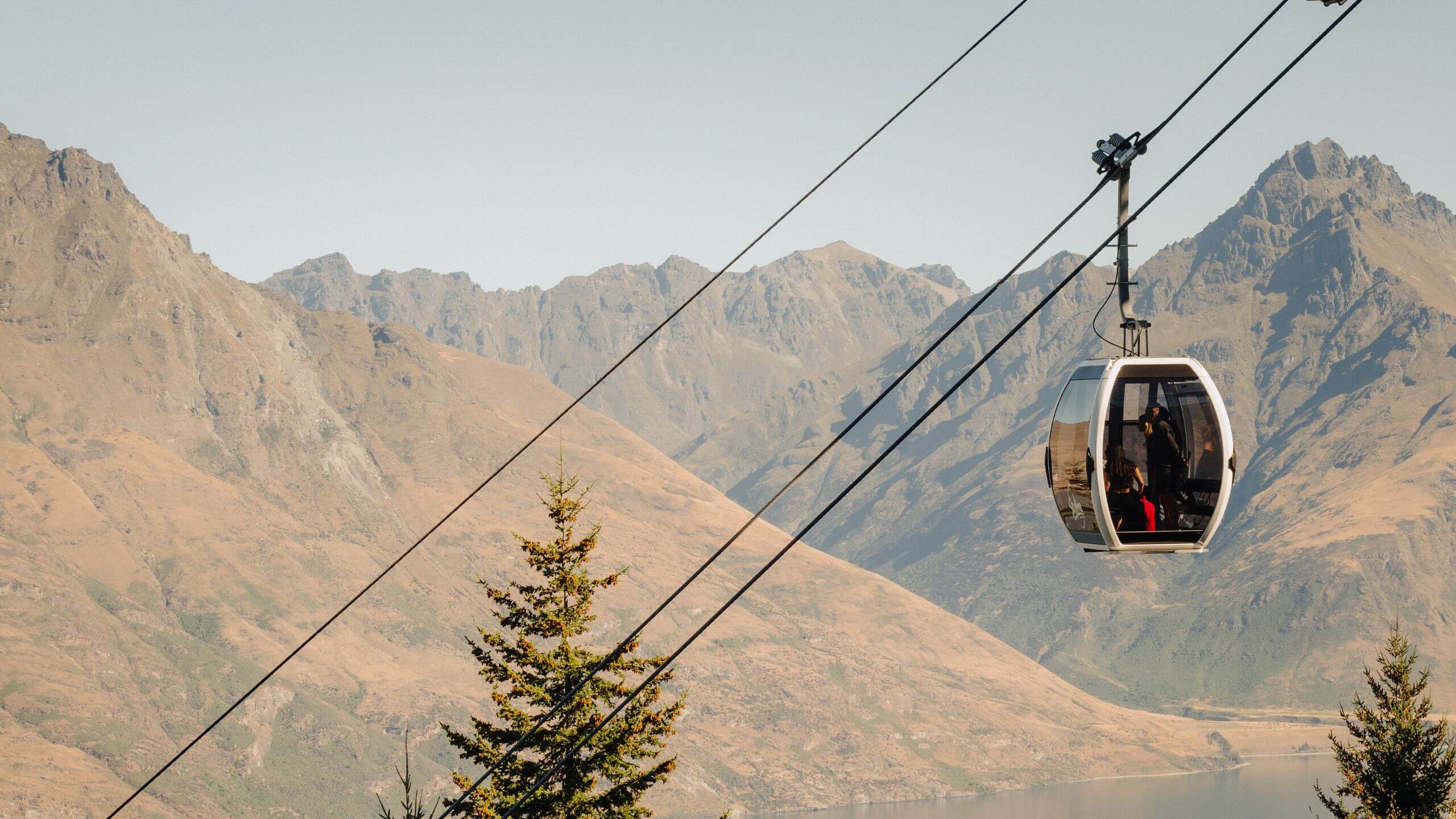 Skyline gondola cabin ascending above Queenstown with Cecil Peak, Walter Peak, and Walter Peak Station visible across Lake Wakatipu.