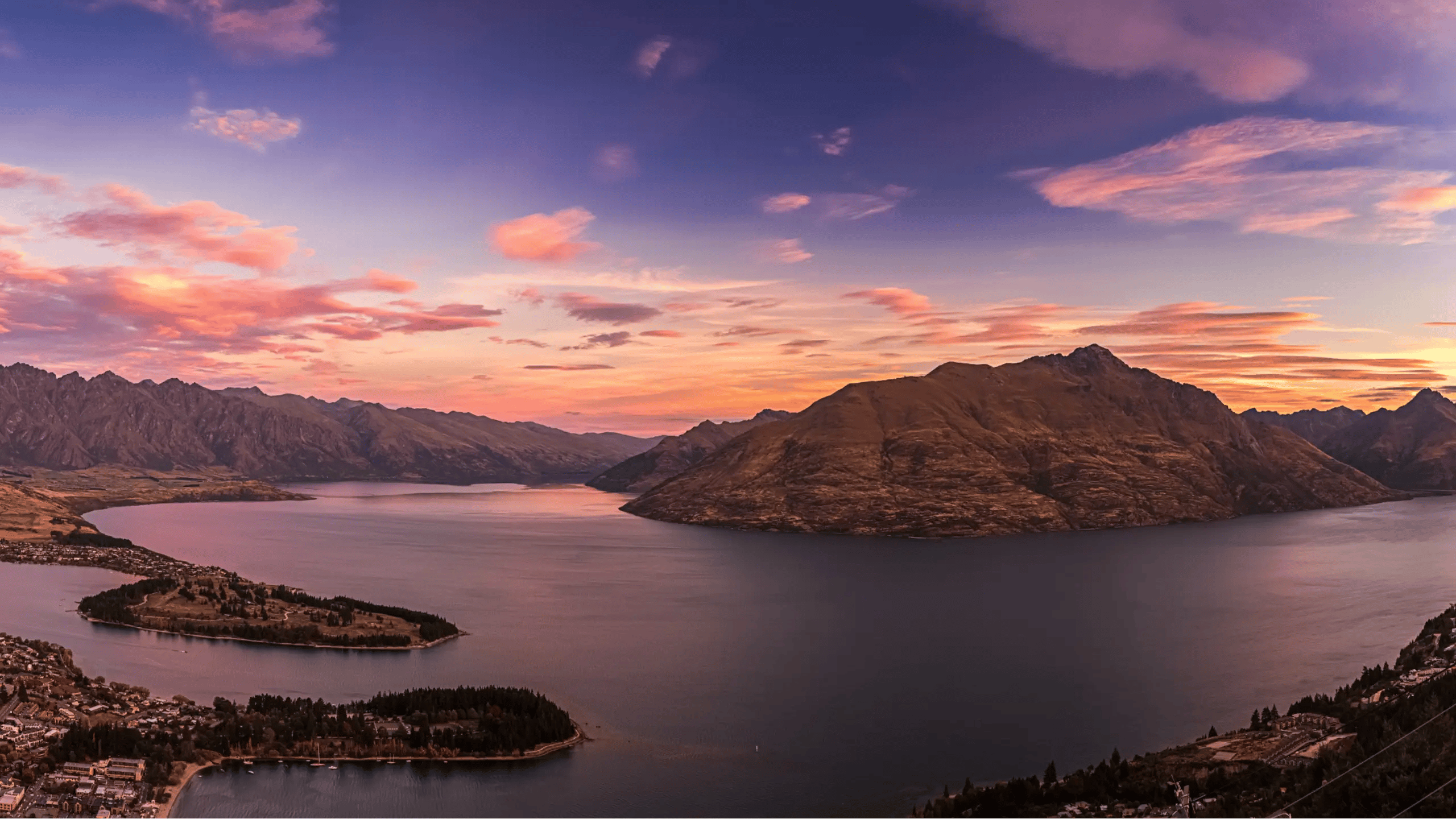 Panoramic sunset view over Queenstown, Lake Wakatipu, and the surrounding mountains from the Skyline Gondola.