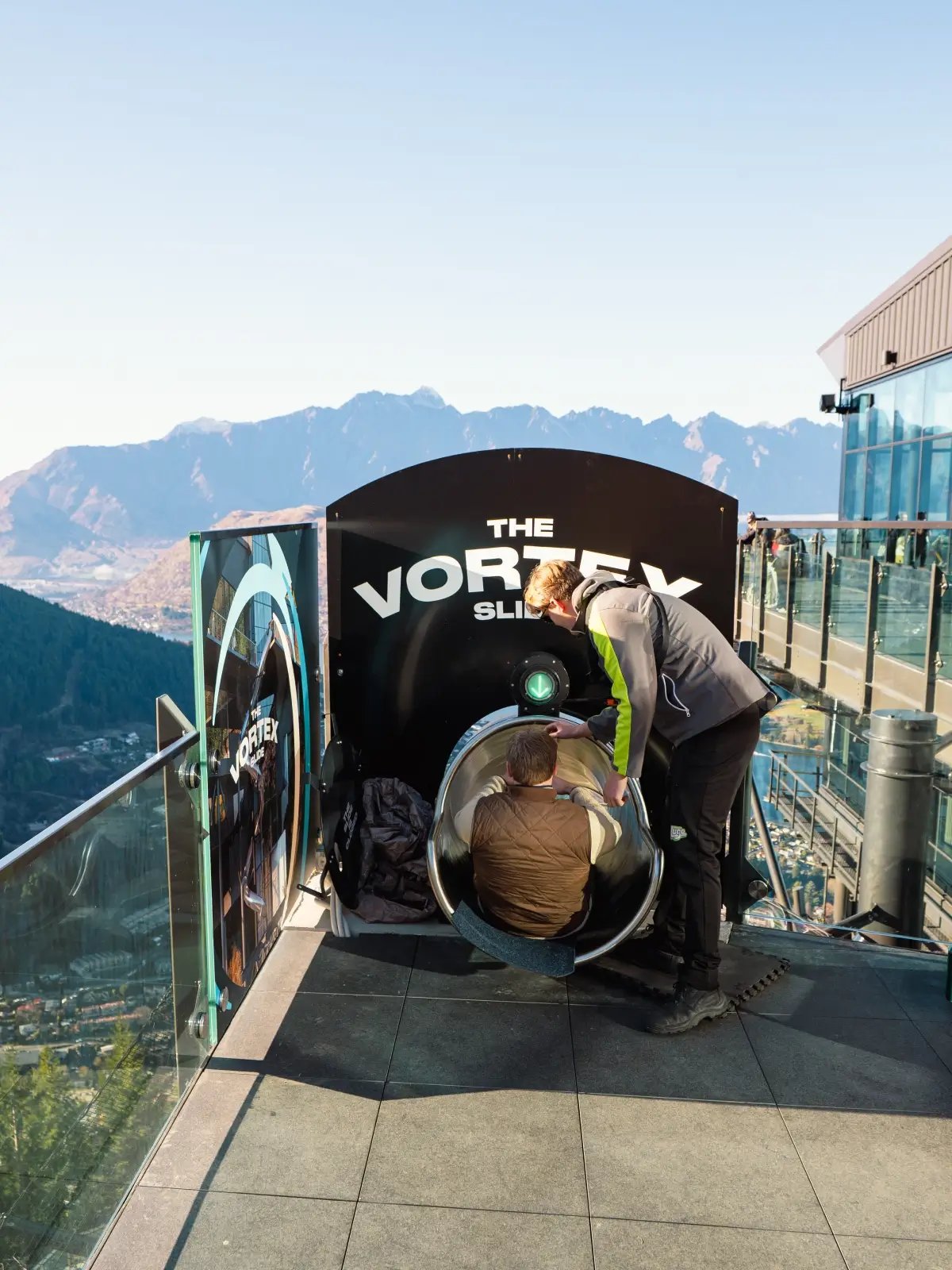 Guest preparing to ride the Skyline Queenstown Vortex Slide with views over Lake Wakatipu and the Remarkables.