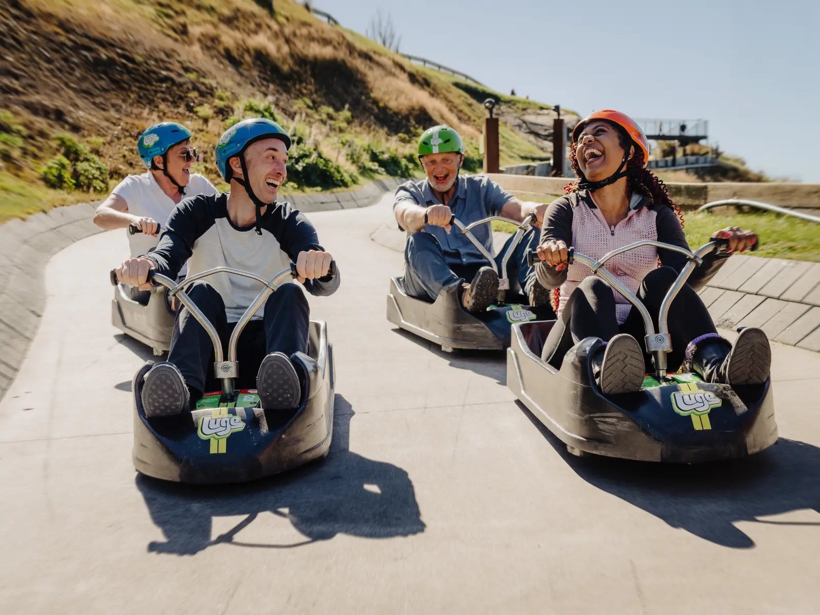 Group of friends riding the Skyline Queenstown Luge side by side and laughing on the track