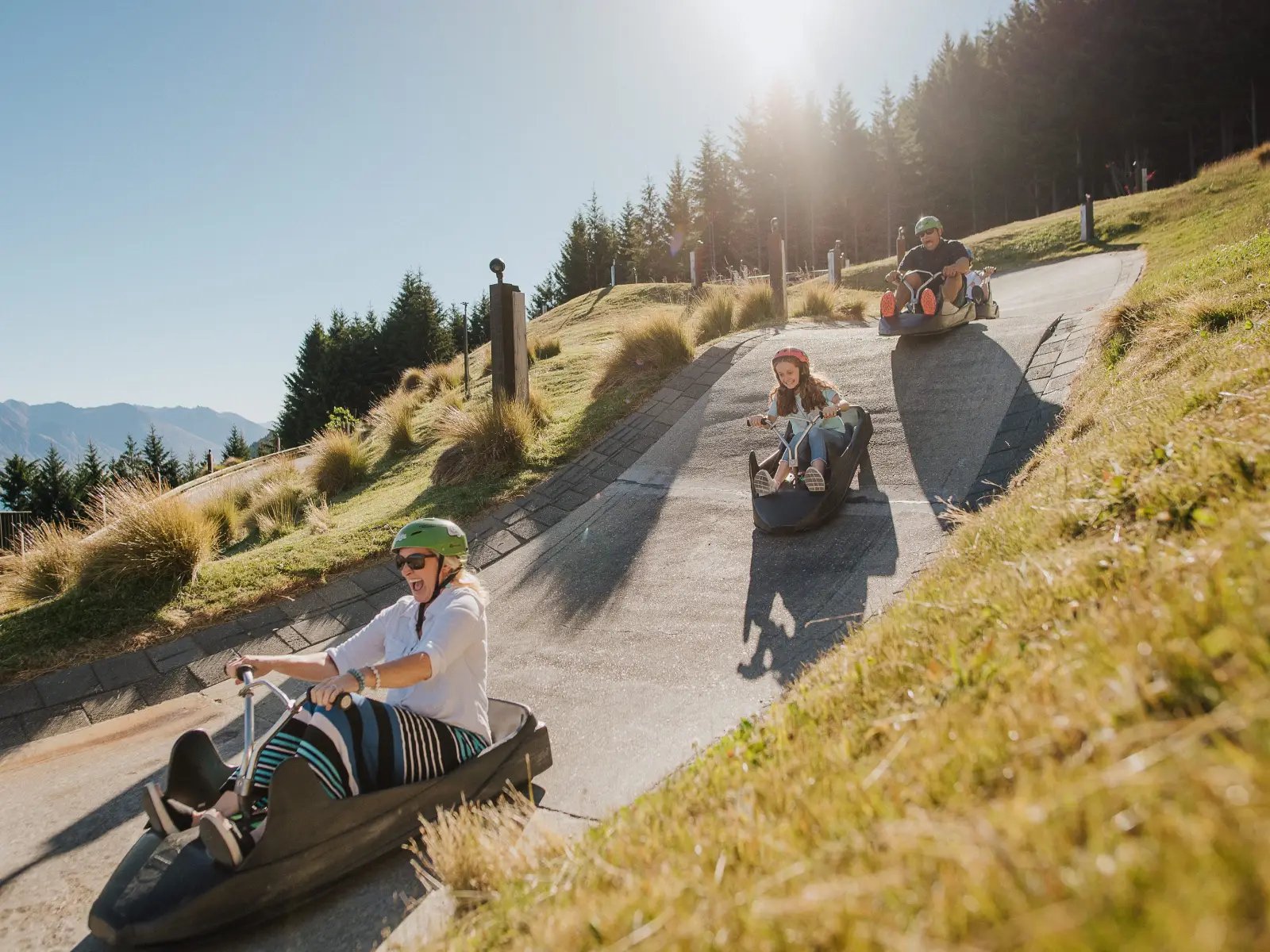 Family riding the Skyline Queenstown Luge downhill on a sunny day with mountain views