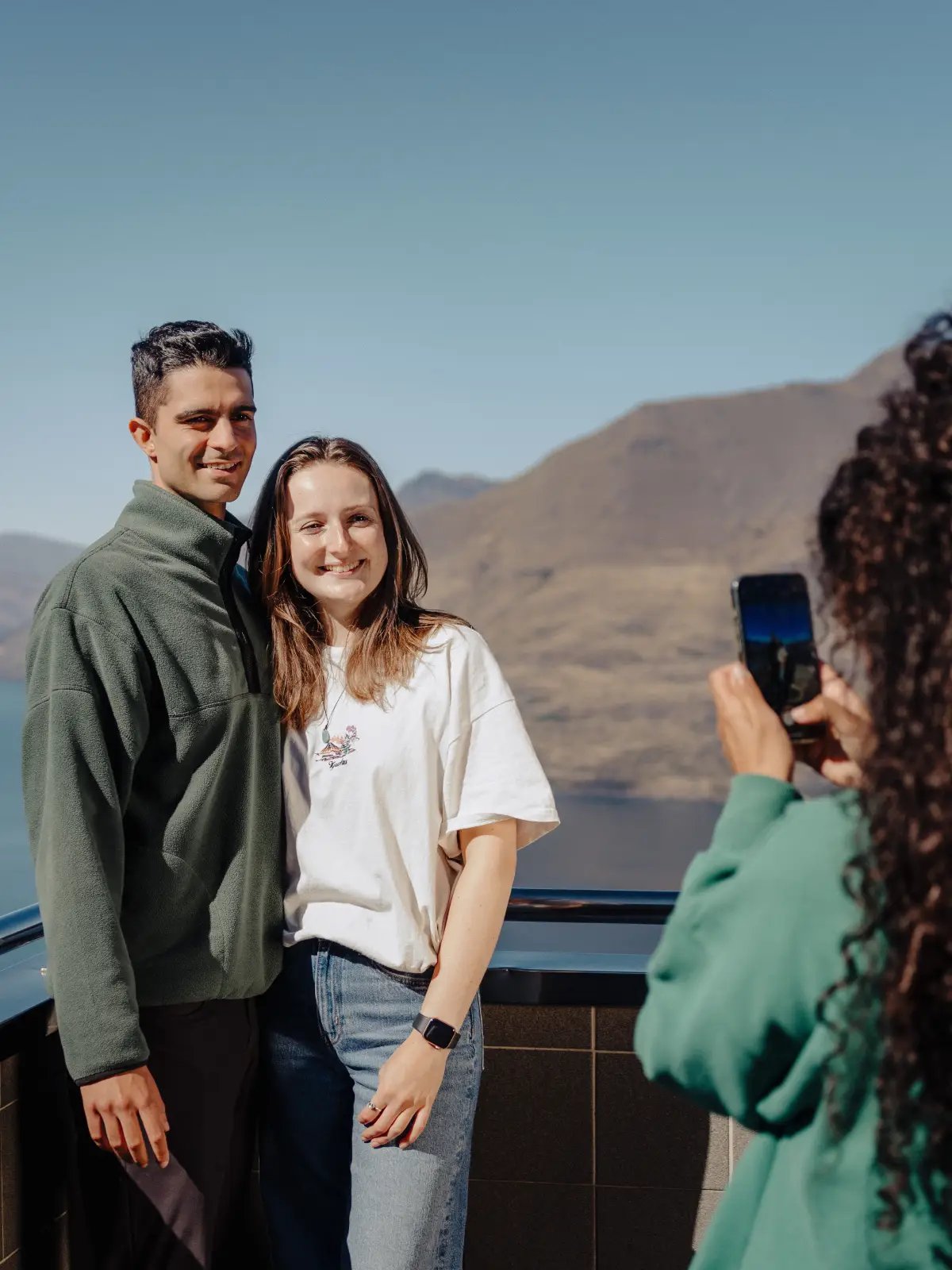Couple posing for a photo at Skyline Queenstown lookout with mountain and lake views in the background