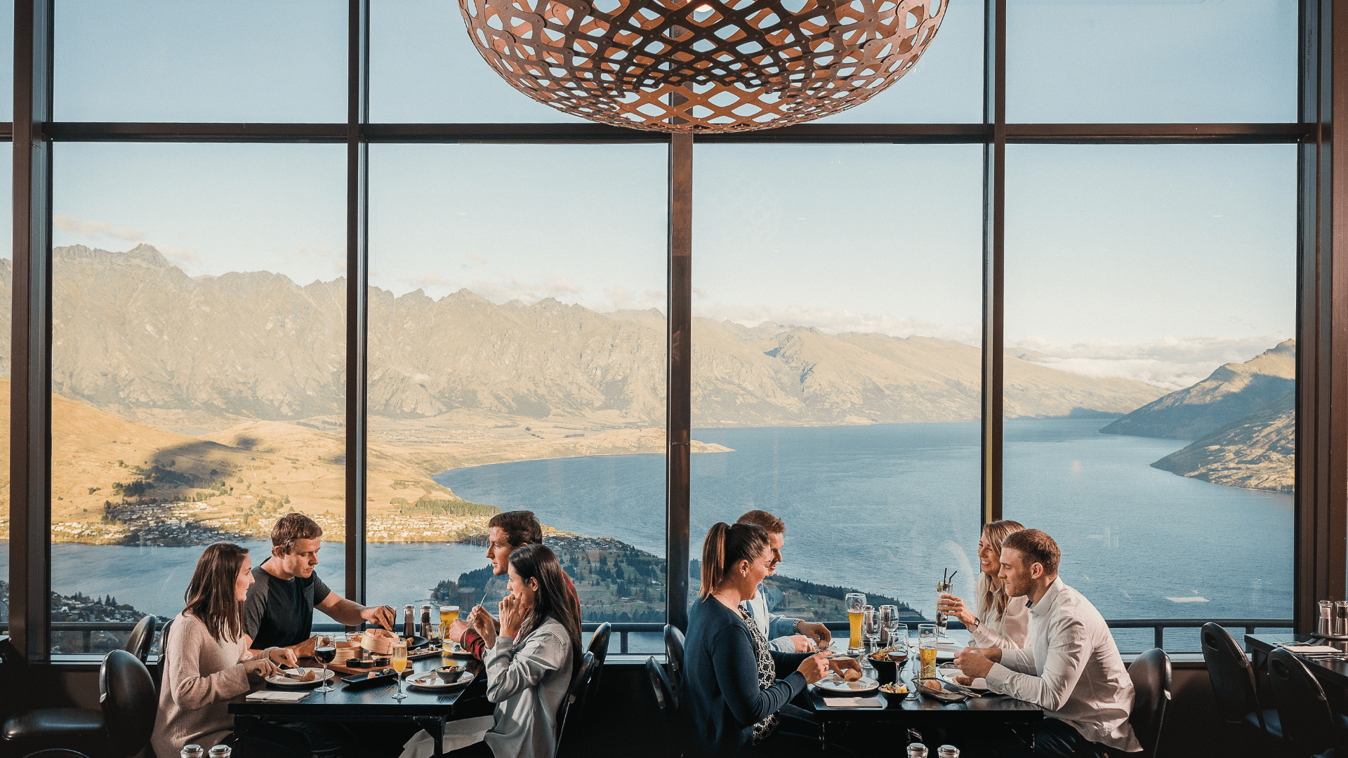Friends dine in the Stratosfare Restaurant at Skyline Queenstown with stunning views of Lake Wakatipu and the surrounding mountains.