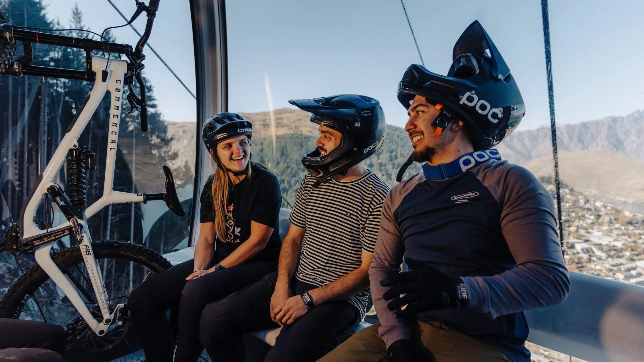 Mountain bikers wearing helmets inside the Skyline Queenstown gondola with bikes and views over Queenstown and surrounding mountains.