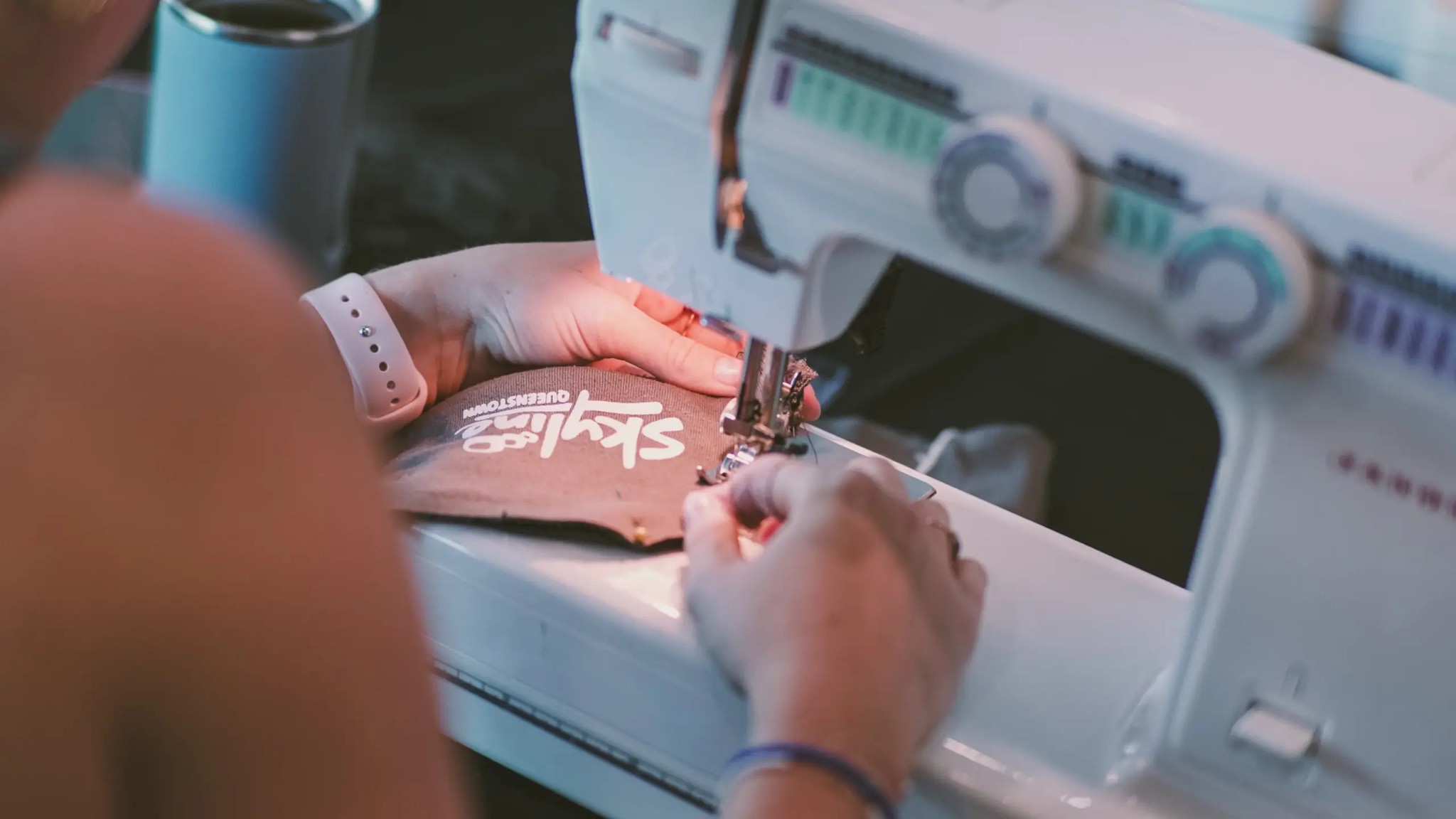 Close-up of repatching a Skyline Queenstown uniform using a sewing machine as part of a textile upcycling initiative.