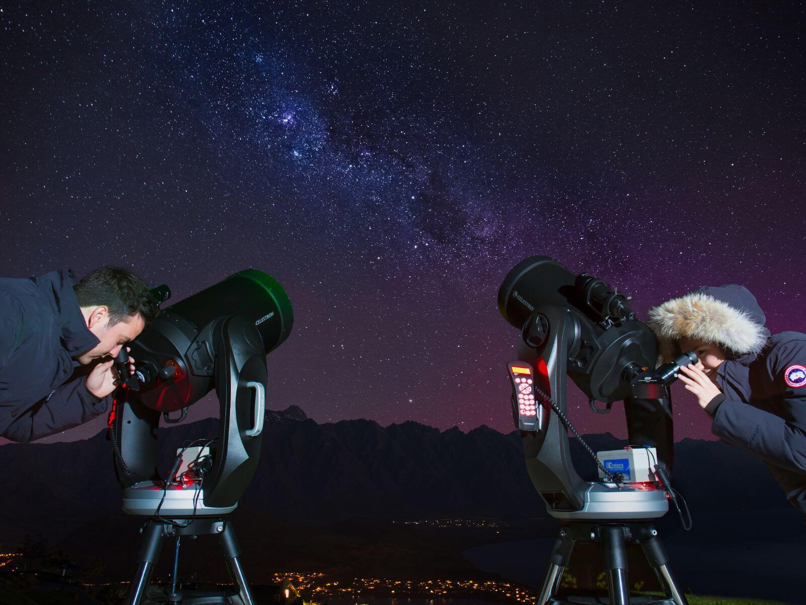 Two people looking through telescopes, with a starry sky in the background