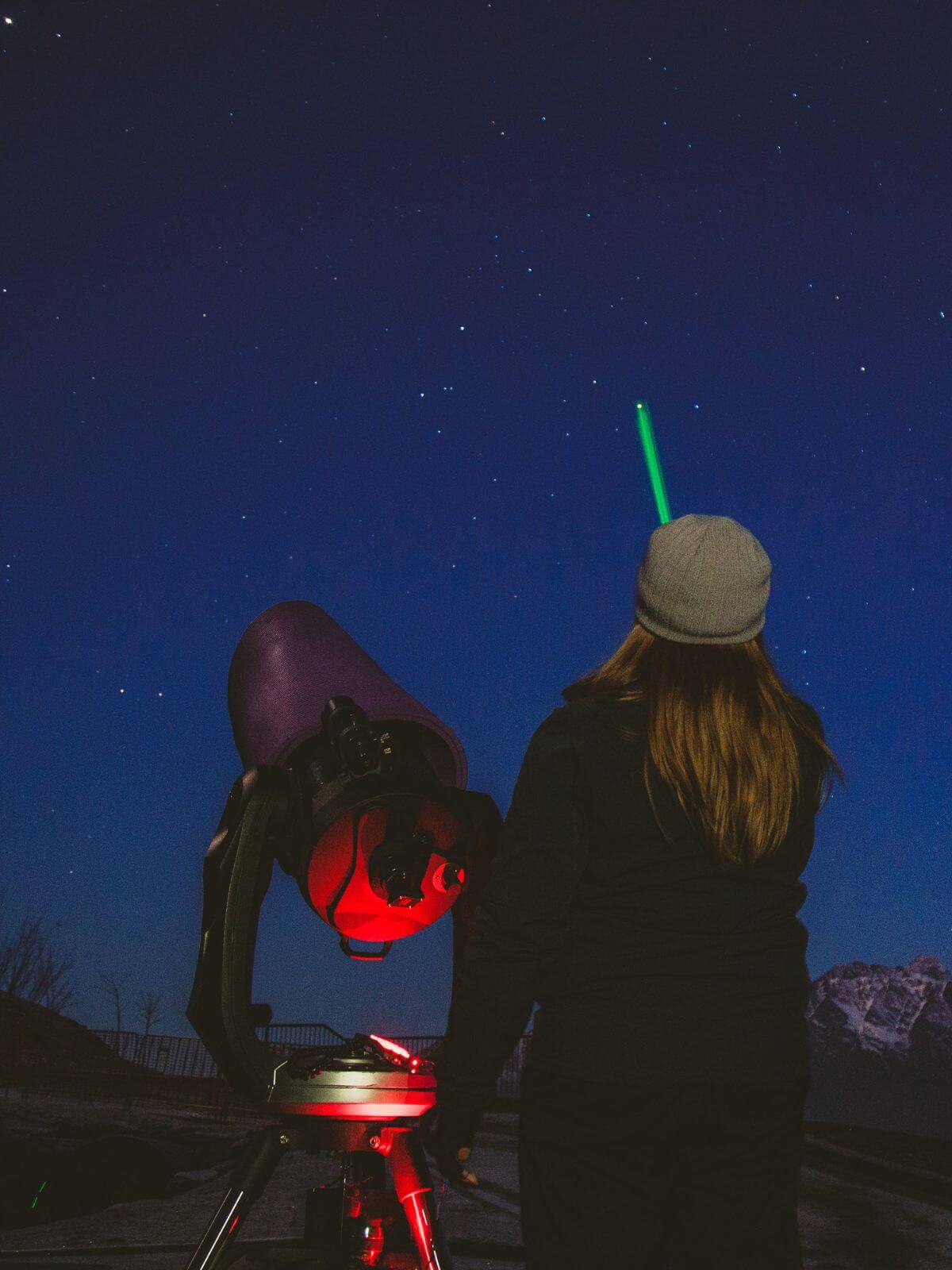 Stargazing guide using a green laser to point out stars in the nights sky with telescope next to her